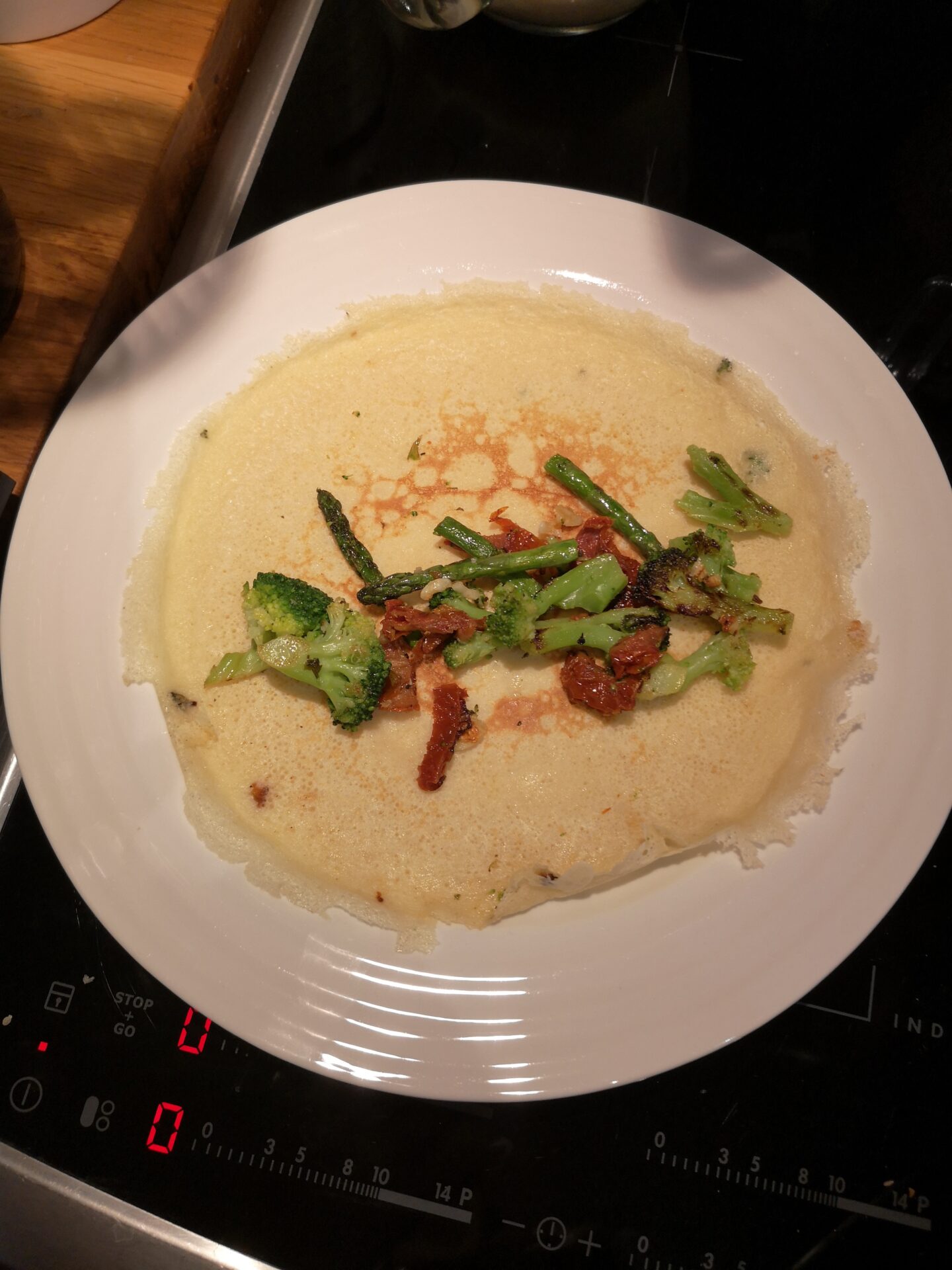 Pancake on the plate, open with the broccoli, asparagus, sundried tomato and garlic laid out down the centre
