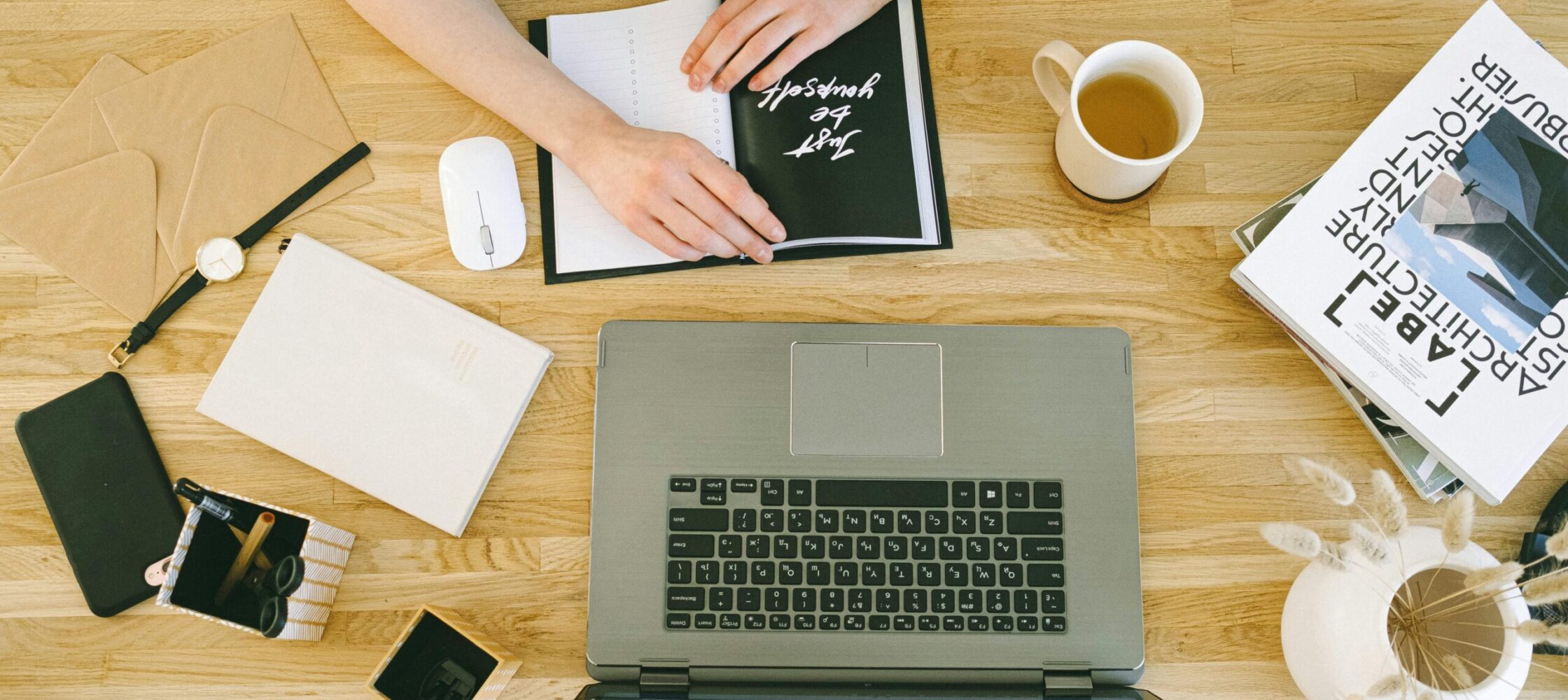Woman working at a laptop with notebook and coffee, flatlay of creative workspace for small business owner writing newsletter – Photo by Ivan Samkov via Pexels
